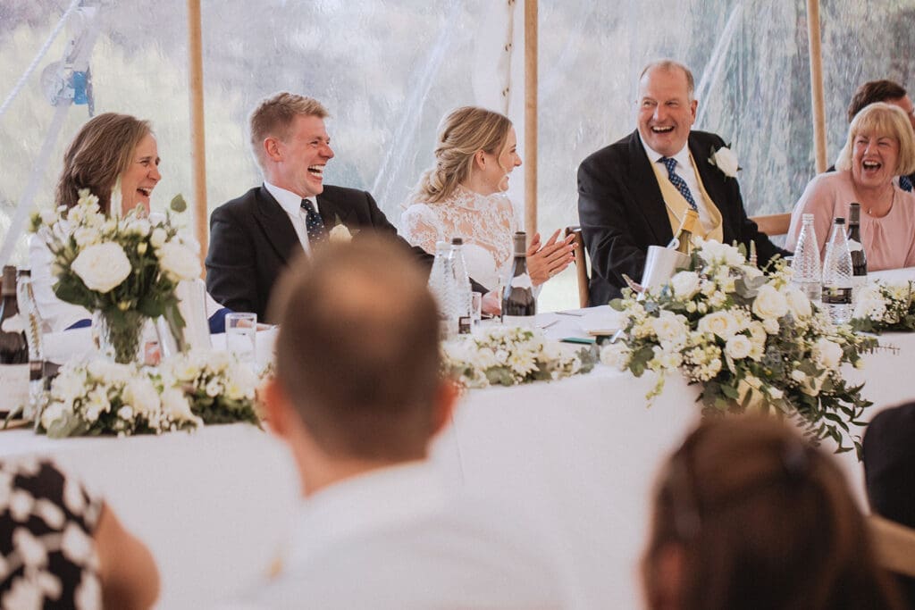 Top table setup with white and green wedding flowers inside marquee